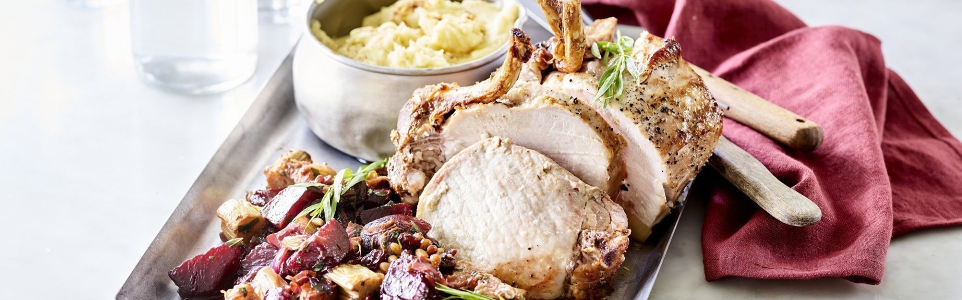 Gebraden varkenskroontje met rabarber, rode biet en dragon Het varkenskroontje ligt op een ovenplaat samen met de stukjes rabarber en rode biet. We serveren hem met een kommetje versgemaakte puree. Er ligt een donkerrode servette bij het gerecht om de rode biet nog meer te accentueren, een herfsttopper!