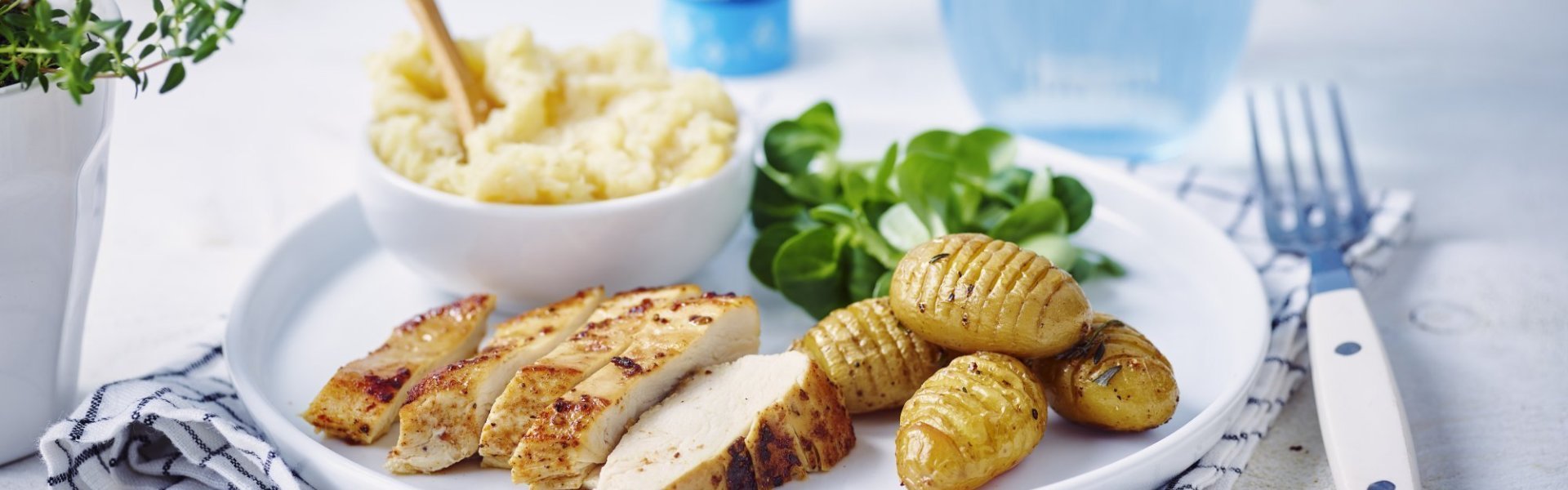 Gebakken kipfilet gesneden in sneetjes en opgediend op een wit groot bord. Naast de kipfilet liggen hasselback potatoes en een appelmoes met pastinaak. 