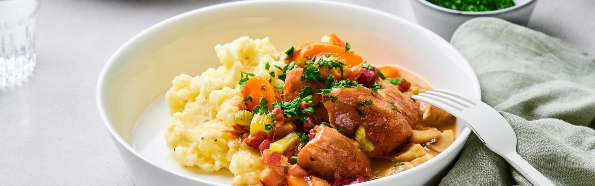 Kalfsfricassee met spekblokjes Op tafel staan twee uitgeschepte porties van het hoofdgerecht. Een schep heerlijke puree met kalfsfricassee. In de fricassee zitten spekblokjes, selder en wortelstukjes. Het gerechtje is afgewerkt met verse peterselie. Er ligt een licht groene servette langs en wit bestek.