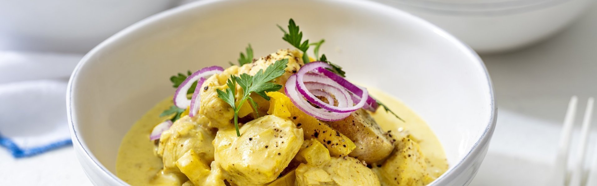 Kip curry met krieltjes Op tafel staan twee porties uitgeschept, om onmiddelijk aan te vallen met mes en vork. De curry kleurt mooi goudgeel, terwijl de rode ui voor contrast zorgt. We werken af met een takje verse peterselie voor extra kleur.