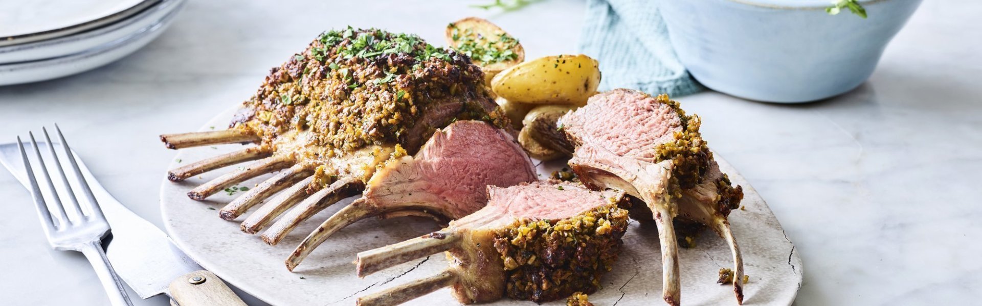 Lamskroon met pittige kruidenkorst en gebakken krieltjes Heerlijke lamskroon met pittige en krokante kruidenkorst ligt klaar om aan te snijden. Ze wordt geserveerd met krielaardappeltjes en apart een slaatje.