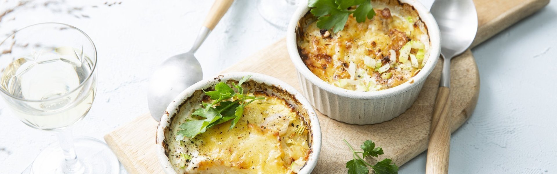 Minigratin met extra groenten Minigratin met aardappel, sjalot, prei, selder en Belgische kaas. Ideaal om te serveren in kleine ovenschaaltjes of -potjes. Deze gratins staan op een houten plankje met 2 glaasjes witte wijn langs.