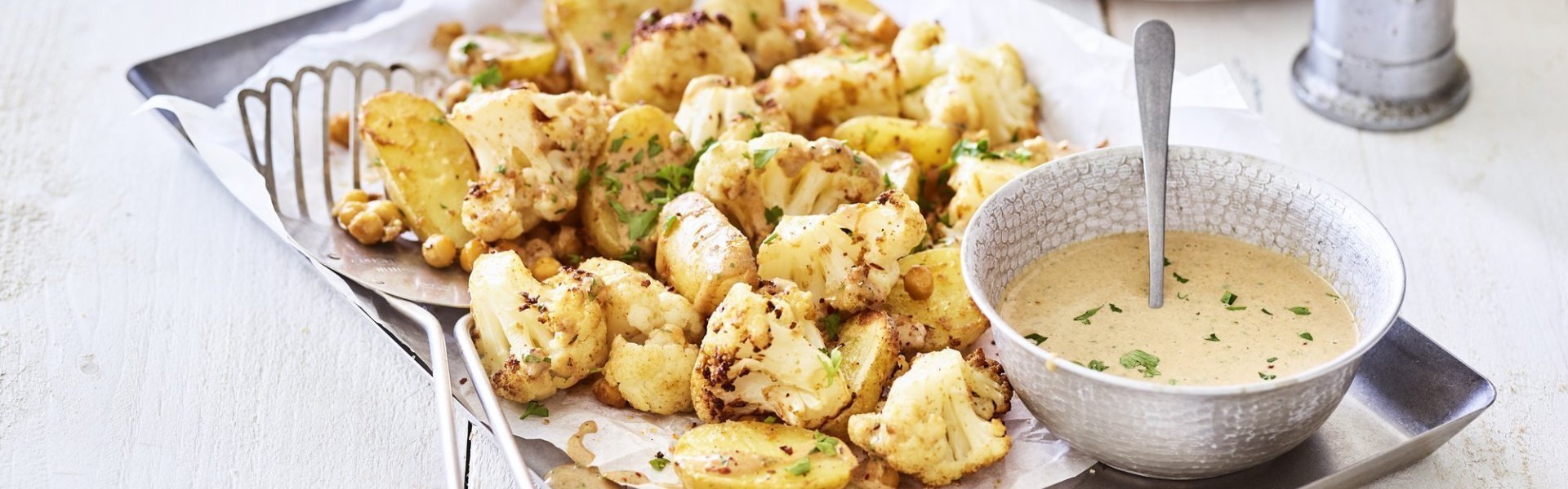 Ovenschotel met kikkererwten, bloemkool en krieltjes Een ovenschotel gevul de goud! Zo ziet hij er eigenlijk een beetje uit. De ovenschotel is bestaat nl uit kleine aardappelen, kikkererwten en bloemkoolroosjes. We dienen hem op met een heerlijk sausje op basis van tahini. Alles afgewerkt met groene snippers van de peterselie.