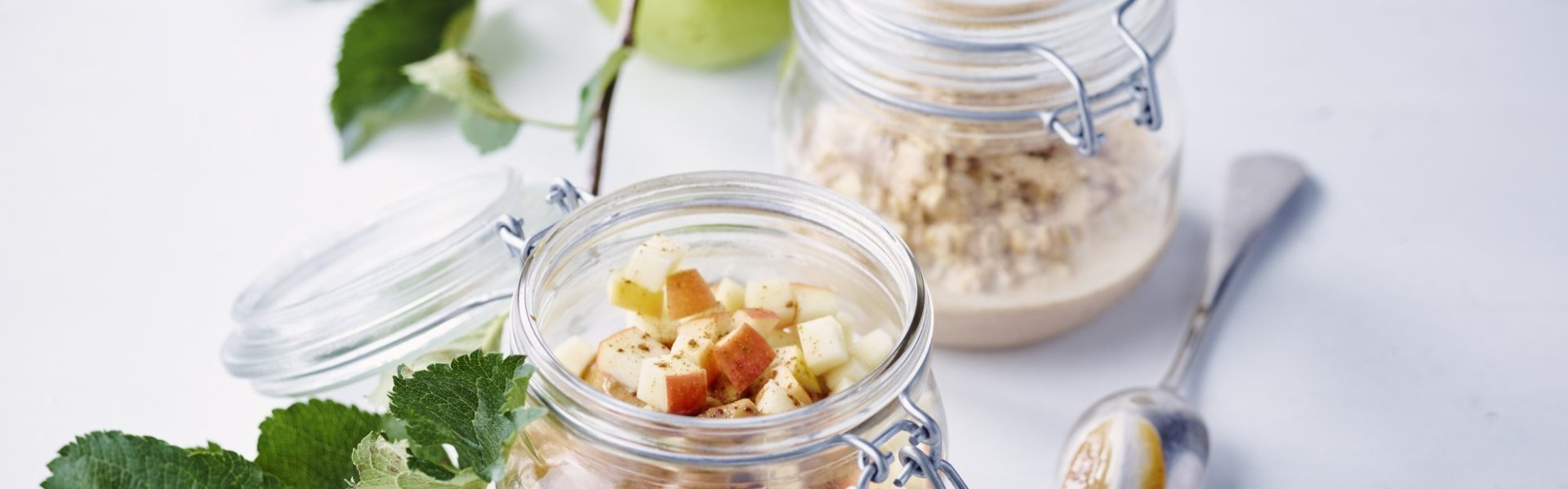 Overnight oats met appel Klaargemaakte havermout in glazen bokaal met stukjes verse appel, pindakaas en kaneelpoeder. Er ligt ook een appeltak met appel op de foto, een Golden van bij ons...