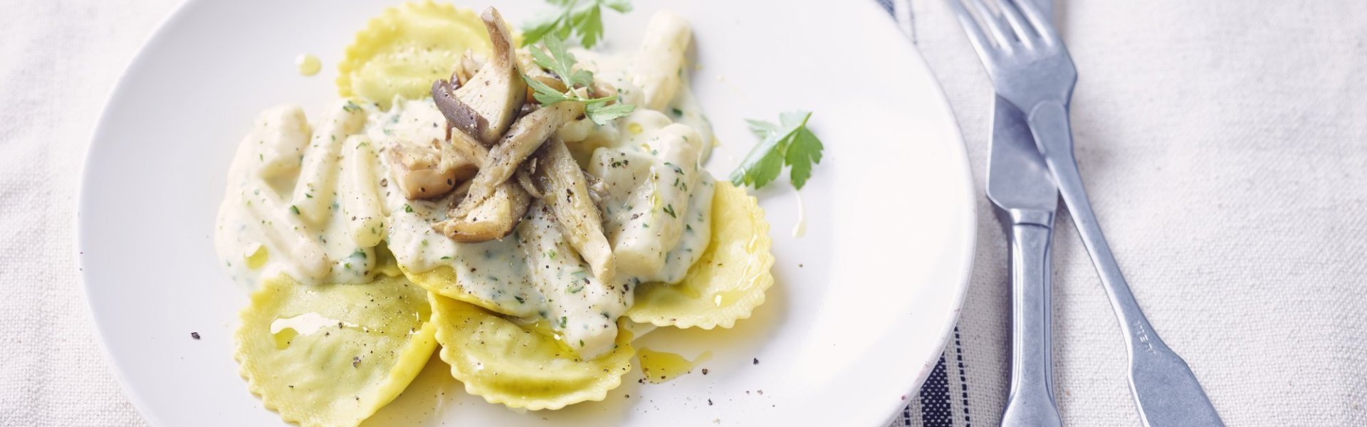 Groot wit bord met ravioli in het midden geschept. Hierop liggen schorseneren met een gladde witte saus afgewerkt met geflambeerde boschampignons.