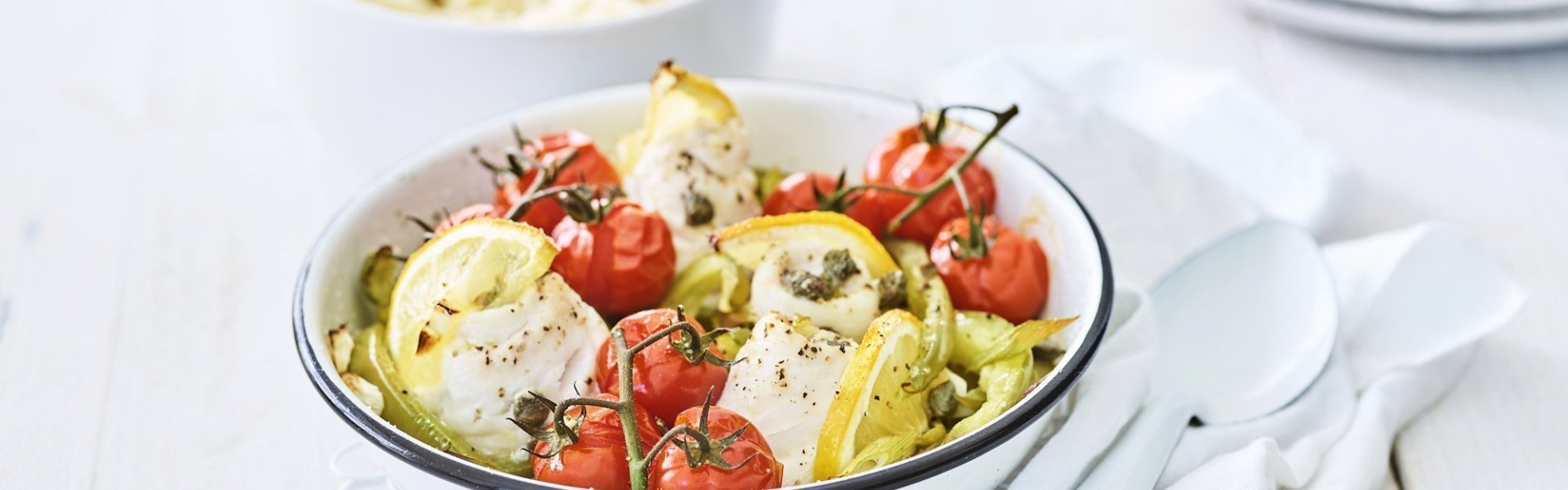 In een ronde ovenschaal liggen de tongrolletjes te blinken. De ovenschotel werd aangevuld met kerstomaatjes in trosvorm en stukjes groene paprika. Er werden ook partjes citroen toegevoegd voor een extra frisse smaak. In de achtergrond is een kommetje gevuld met puree.