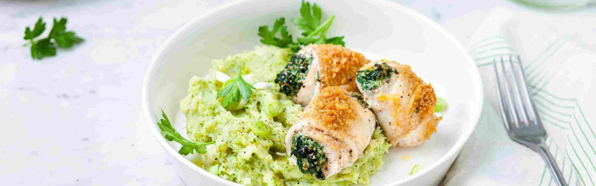 Tongrolletjes met broccolipuree Gevulde tongrolletjes met spinazie en ricotta liggen op een groene puree van broccoli en aardappel. Ze liggen in een diep bord waarbij een karaf- en waterglas langs staat.