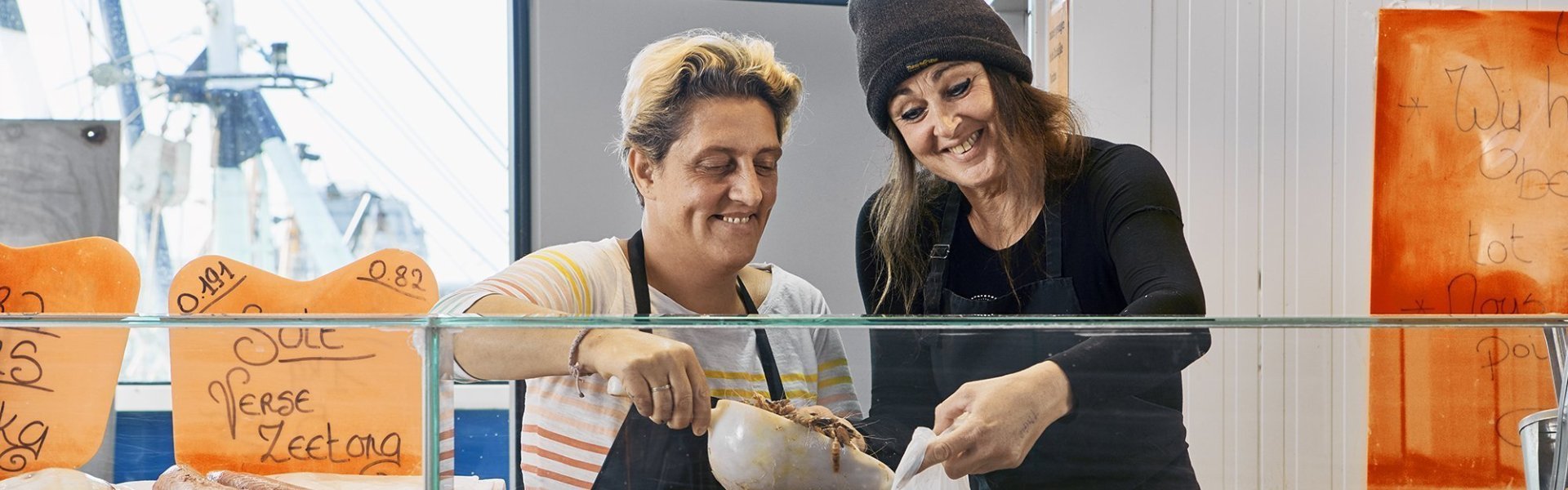 Twee vrouwen staan aan de vistoog in de vistrap. Ze scheppen verse garnalen in witte zak. Echte vissersvrouwen met een hart voor verse vis.