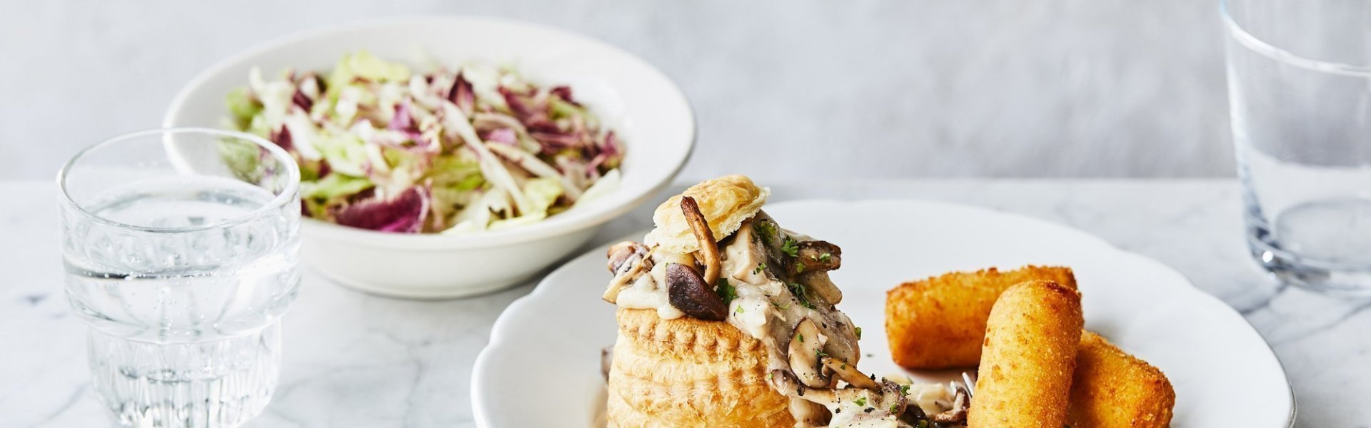 Een heerlijke vol-au-vent in met goudgele kroketten op een bord geserveerd. Er ligt een vork op het bord en het slaatje op basis van radicchio staat bovenaan, dat zorgt voor extra kleur. 