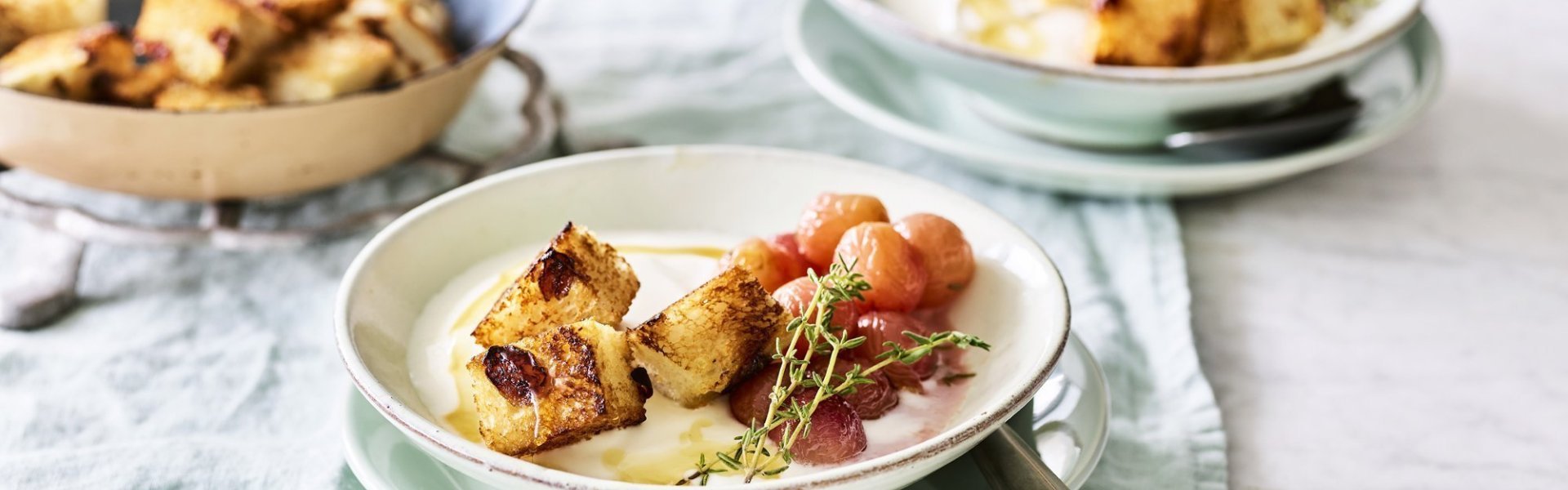 Yoghurt met gegrilde druiven en croutons Een heerlijk én makkelijk ontbijtje staat klaar op tafel. De yoghurt is geserveerd in ontbijtkommetjes en afgewerkt met gegrilde druiven en krokante croutons van rozijnenbrood.