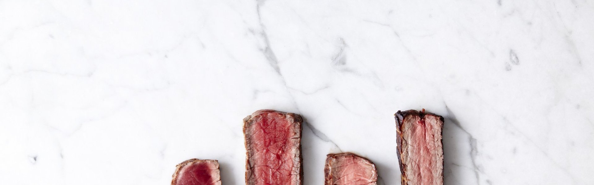 Reepjes steak liggen op een marmere ondergrond, de steak is te zien in zijn 4 cuissons. Bleu, saignant, a point en bien cuit.