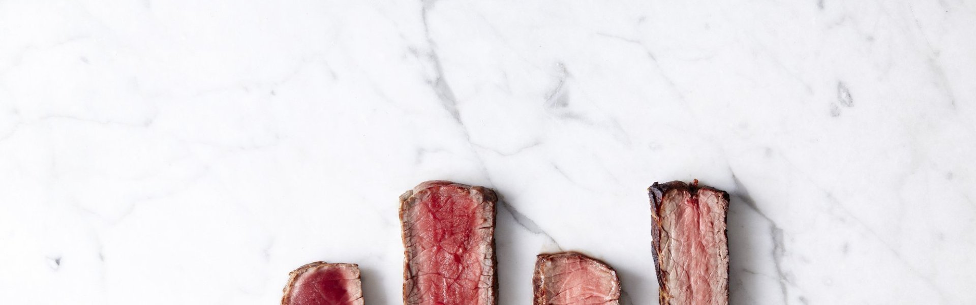 Bakwijze steak Reepjes steak liggen op een marmere ondergrond, de steak is te zien in zijn 4 cuissons. Bleu, saignant, a point en bien cuit.