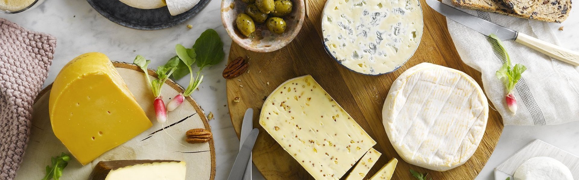 kaasschotel met hartige zuiderse toets Kaasschotel op marmeren keukenblad. Verschillende Belgische kazen liggen op houten planken met brood, noten, radijzen en chutney erbij.