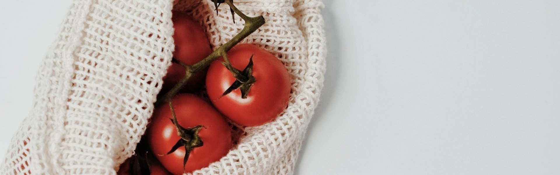 Tomaten in groentennetje Trostomaten op het keukenaanrecht samen met een houten lepel en groentennetje met extra tomaten.