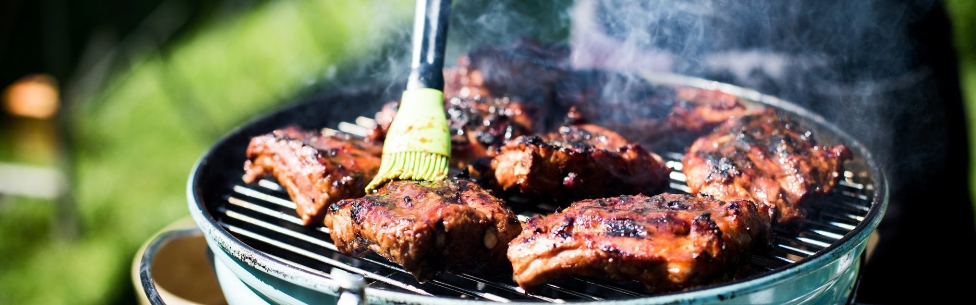 Ribbetjes op een barbecue in de tuin. De kok borstel nog wat marinade op het vlees.